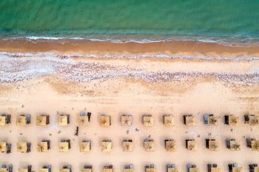 Aerial view of a beach with wooden umbrellas, and calm sea.
