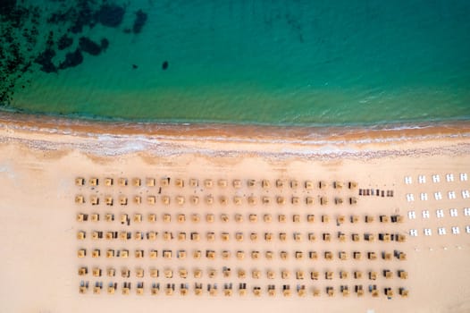 Aerial view of an stunning beach with wooden umbrellas, and calm sea.