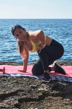 Latin woman, middle-aged, wearing sportswear, training, doing physical exercises, plank, sit-ups, climber's step, burning calories, keeping fit, outdoors by the sea, wearing headphones, smart watch