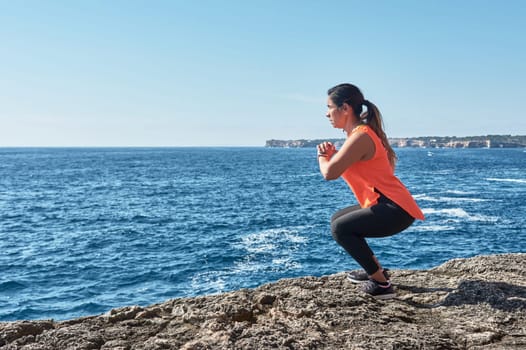 Latin woman, middle-aged, wearing sportswear, training, doing physical exercises, plank, sit-ups, climber's step, burning calories, keeping fit, outdoors by the sea, wearing headphones, smart watch