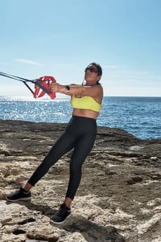 Latin woman, middle-aged, wearing sportswear, training, doing physical exercises, plank, sit-ups, climber's step, burning calories, keeping fit, outdoors by the sea, wearing headphones, smart watch