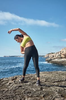 Latin woman, middle-aged, wearing sportswear, training, doing physical exercises, plank, sit-ups, climber's step, burning calories, keeping fit, outdoors by the sea, wearing headphones, smart watch