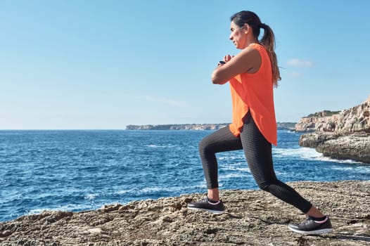 Latin woman, middle-aged, wearing sportswear, training, doing physical exercises, plank, sit-ups, climber's step, burning calories, keeping fit, outdoors by the sea, wearing headphones, smart watch