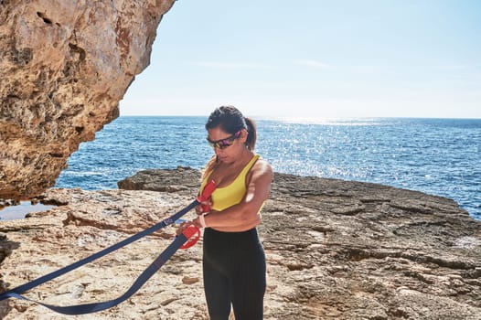 Latin woman, middle-aged, wearing sportswear, training, doing physical exercises, plank, sit-ups, climber's step, burning calories, keeping fit, outdoors by the sea, wearing headphones, smart watch