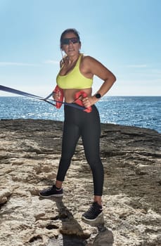 Latin woman, middle-aged, wearing sportswear, training, doing physical exercises, plank, sit-ups, climber's step, burning calories, keeping fit, outdoors by the sea, wearing headphones, smart watch