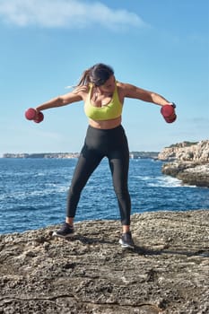 Latin woman, middle-aged, wearing sportswear, training, doing physical exercises, plank, sit-ups, climber's step, burning calories, keeping fit, outdoors by the sea, wearing headphones, smart watch