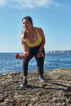 Latin woman, middle-aged, wearing sportswear, training, doing physical exercises, plank, sit-ups, climber's step, burning calories, keeping fit, outdoors by the sea, wearing headphones, smart watch