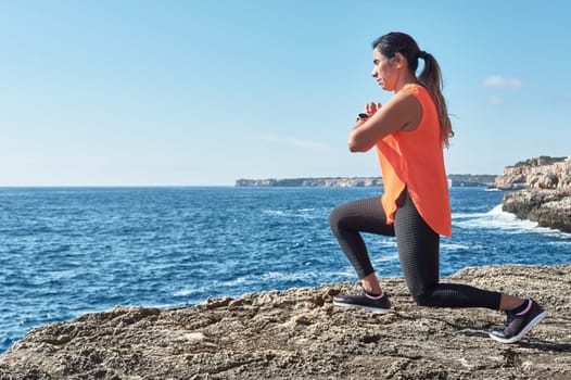 Latin woman, middle-aged, wearing sportswear, training, doing physical exercises, plank, sit-ups, climber's step, burning calories, keeping fit, outdoors by the sea, wearing headphones, smart watch