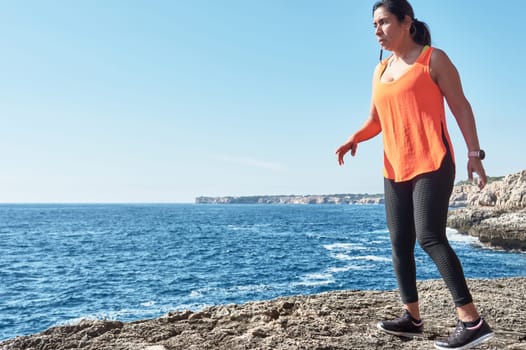 Latin woman, middle-aged, wearing sportswear, training, doing physical exercises, plank, sit-ups, climber's step, burning calories, keeping fit, outdoors by the sea, wearing headphones, smart watch
