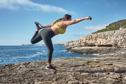 Latin woman, middle-aged, wearing sportswear, training, doing physical exercises, plank, sit-ups, climber's step, burning calories, keeping fit, outdoors by the sea, wearing headphones, smart watch