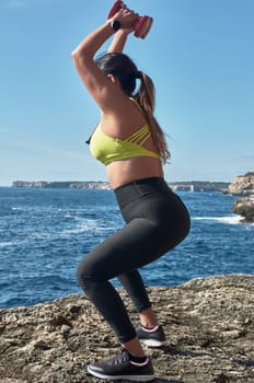 Latin woman, middle-aged, resting, regaining strength, eating, drinking water, after a gym session, burning calories, keeping fit, outdoors by the sea, wearing headphones and smart watch