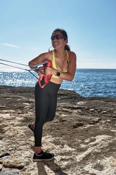 Latin woman, middle-aged, wearing sportswear, training, doing physical exercises, plank, sit-ups, climber's step, burning calories, keeping fit, outdoors by the sea, wearing headphones, smart watch