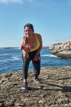 Latin woman, middle-aged, wearing sportswear, training, doing physical exercises, plank, sit-ups, climber's step, burning calories, keeping fit, outdoors by the sea, wearing headphones, smart watch,