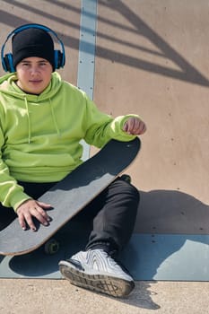 young man, teenager, skateboarding, sitting on the track, wearing headphones, green sweatshirt, black hat, thinking,