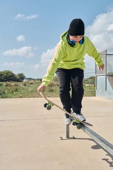 young, teenager, with a skateboard, holding the board with the hand, to jump, on a track, skateboarding, wearing headphones, green sweatshirt, black hat, swinging