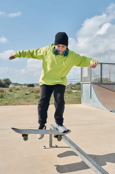 young, teenager, skateboarding, jumping, on the rink, wearing headphones, green sweatshirt, black hat, swinging