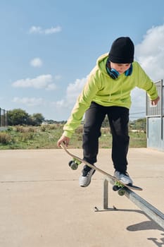 young, teenager, with a skateboard, holding the board with the hand, to jump, on a track, skateboarding, wearing headphones, green sweatshirt, black hat, swinging