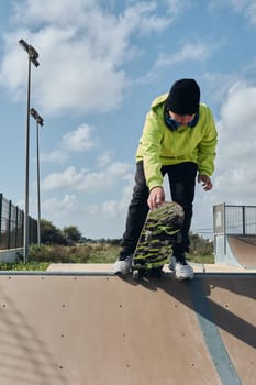 young, teenager, with a skateboard, holding the board with the hand, to launch down the slope, on a track, skateboarding, wearing headphones, green sweatshirt, black hat, swinging