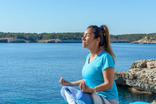 middle-aged fitness woman outdoors in front of the sea does yoga stretching exercises.