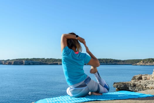 middle-aged fitness woman outdoors in front of the sea does yoga stretching exercises.