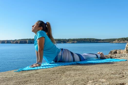 middle-aged fitness woman outdoors in front of the sea does yoga stretching exercises.