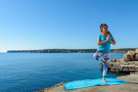 middle-aged fitness woman outdoors in front of the sea does yoga stretching exercises.