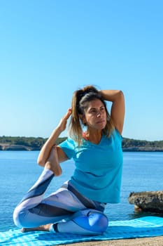 middle-aged fitness woman outdoors in front of the sea does yoga stretching exercises.