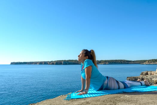 middle-aged fitness woman outdoors in front of the sea does yoga stretching exercises.