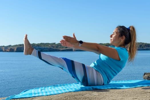 middle-aged fitness woman outdoors in front of the sea does yoga stretching exercises.