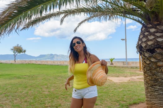 portrait of a latin woman smiling, having fun, on vacation in mallorca posing on a warm spring summer day, under a palm tree, hollidays concept,
