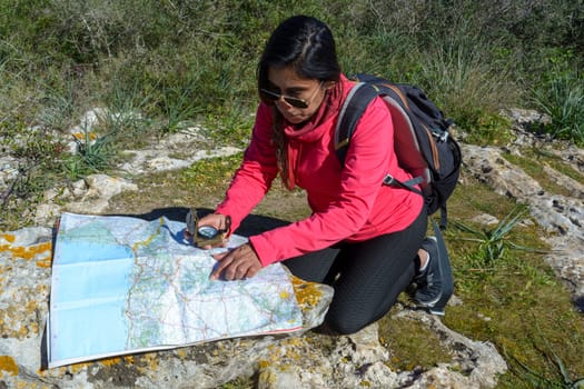 Young hikers sitting on the ground looking at an old map with a compass. Hiking couple in nature