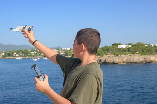 happy teenage boy, preparing and finalizing flight details for drone flight during sunny day with the mediterranean sea in the background Spain, Balearic Islands