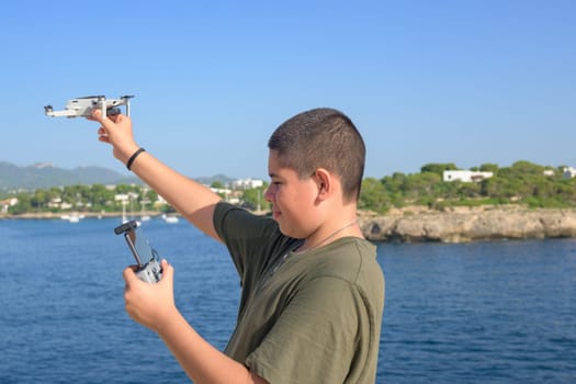 portrait happy teenage boy, preparing and finalizing flight details for drone flight, Mediterranean sea background on a sunny day, technology concept Spain, Balearic Islands