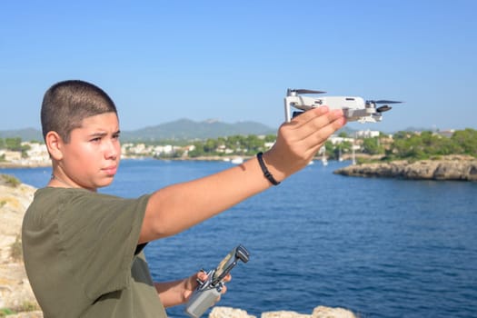 portrait happy teenage boy, preparing and finalizing flight details for drone flight, Mediterranean sea background on a sunny day, technology concept Spain, Balearic Islands