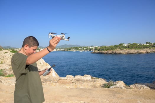 happy teenage boy, preparing and finalizing flight details for drone flight during sunny day with the mediterranean sea in the background Spain, Balearic Islands