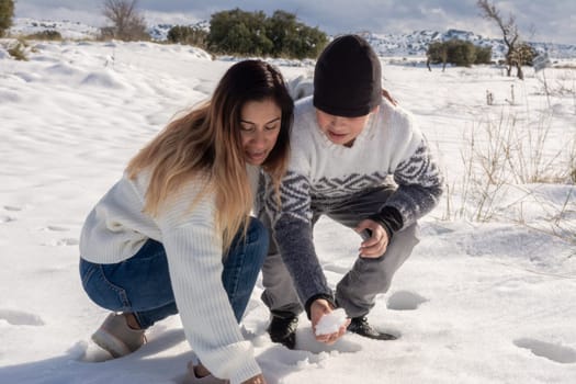 mother and son playing with snowballs in snowy field ,