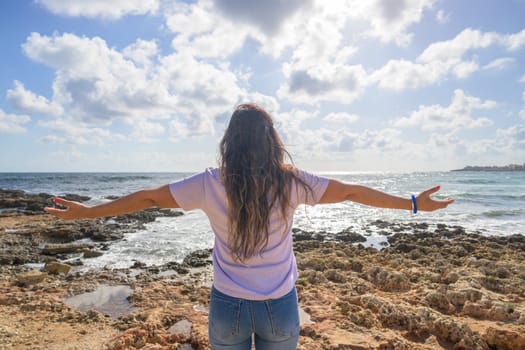 Middle-aged woman stretching her arms breathing fresh air on the Mediterranean coast in front of the sun.,