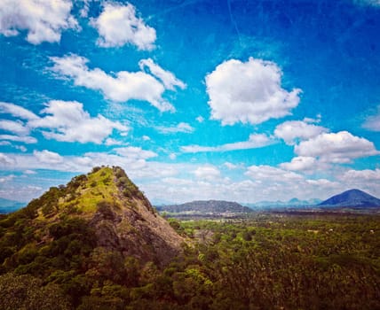 Vintage retro hipster style travel image of sky above small mountains, covered with trees with grunge texture overlaid. Sri Lanka