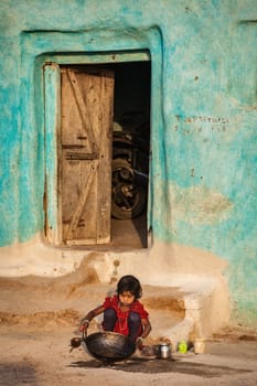 KHAJURAHO, INDIA - APRIL 15, 2011: Unidentified girl cleaning kitchen cooking pan in village street. Child labour is still comon in India