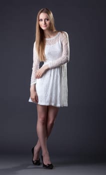 Beautiful tall model posing in white lace dress, on gray background