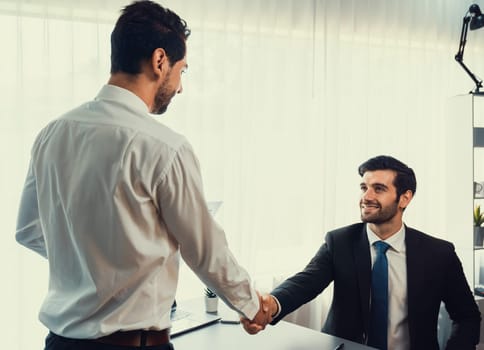 Business partnership meeting with successful trade agreement with handshake or greeting in corporate office desk. Businessman in black suit shaking hand after finalized business deal. Fervent