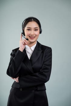 Attractive asian female call center operator with happy smile face advertises job opportunity on empty space, wearing a formal suit and headset on customizable isolated background. Enthusiastic