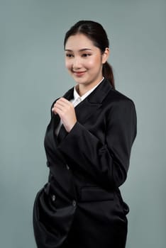 Confident young businesswoman stands on isolated background, posing in formal black suit. Office lady or manager with smart and professional appearance. Enthusiastic
