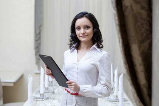 Portrait of smiling waitress posing with menu in hotel restaurant