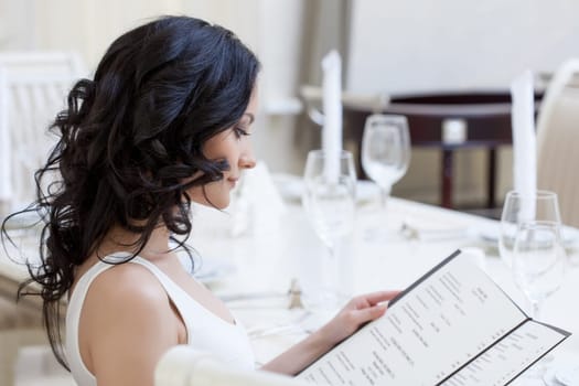 Portrait of curly young brunette choosing dishes from menu