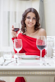 Smiling brunette posing in red dress sits at table
