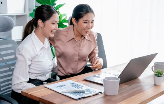 Two young office lady colleagues collaborating in modern office workspace, engaging in discussion and working together on laptop, showcasing their professionalism as modern office worker. Enthusiastic