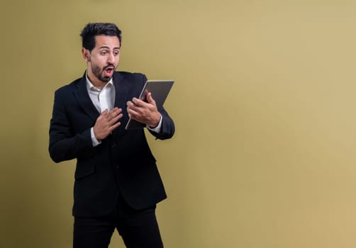 Confident businessman in formal suit holding tablet with surprise look for promotion or advertising. Facial expression and gestures indicate excitement and amazement on an isolated background. Fervent