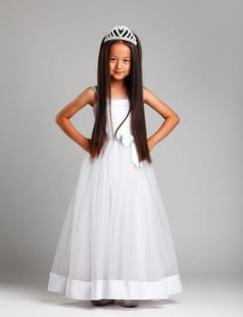 Cute little brunette in elegant dress and crown, on gray background