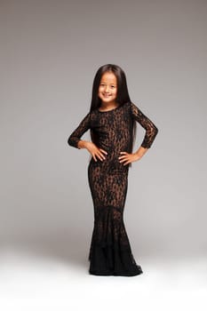 Image of smiling little girl posing in black lace dress, on gray background